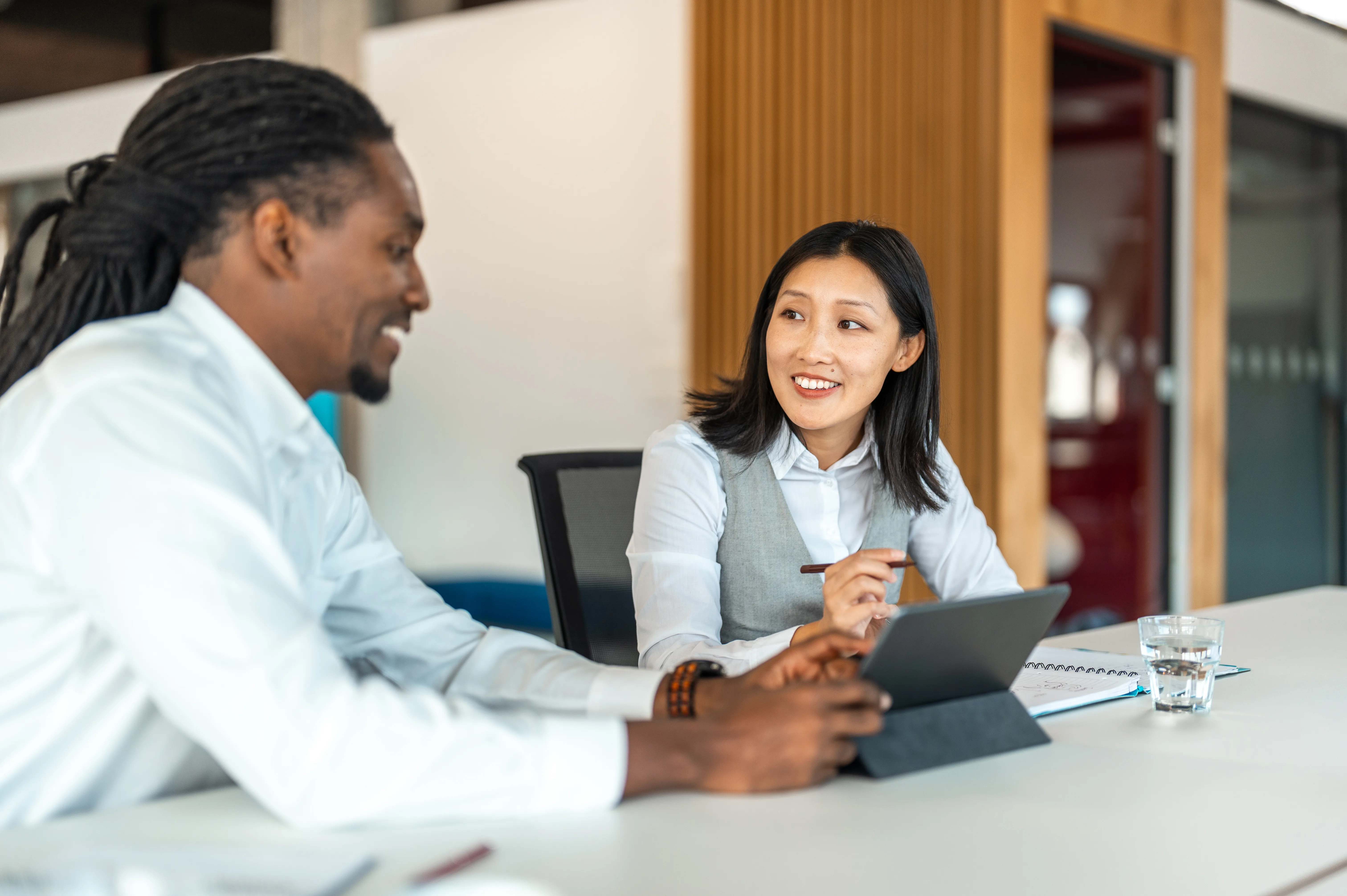 A man and a woman smile and talk with a tablet at an office table