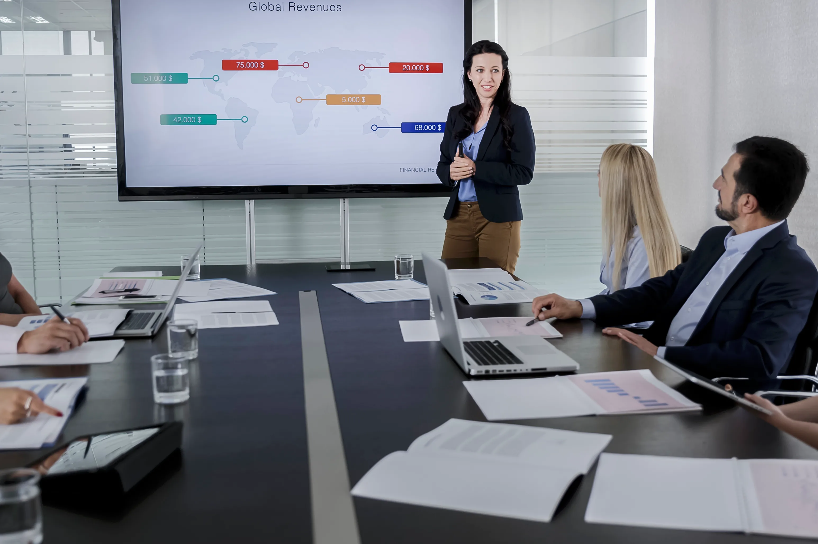 Woman presents a global revenues chart to colleagues seated around a conference table