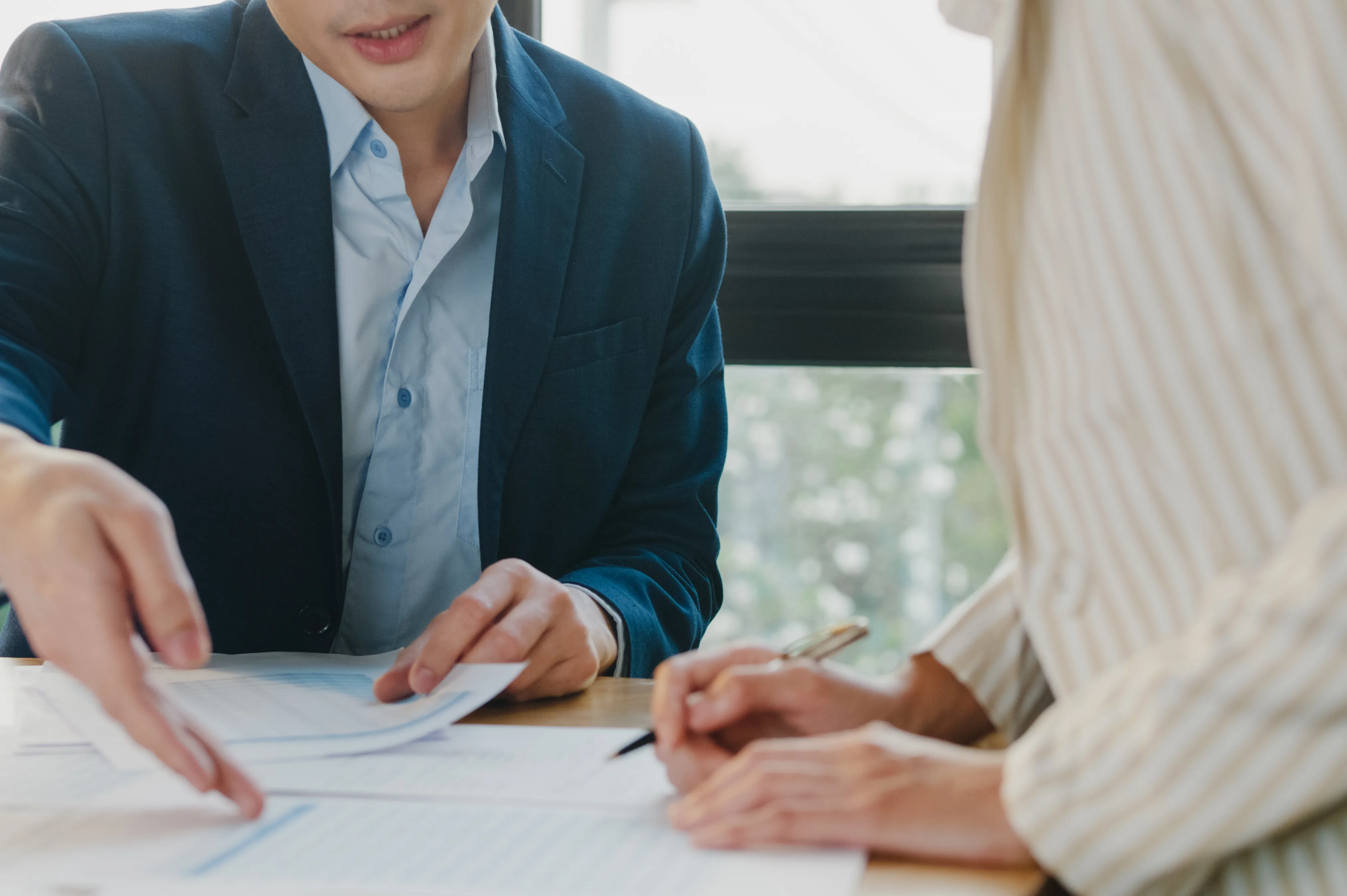 Man in a navy blazer points at a printed chart while a colleague writes notes