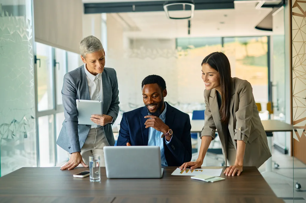 Three colleagues smiling around a laptop in a modern office
