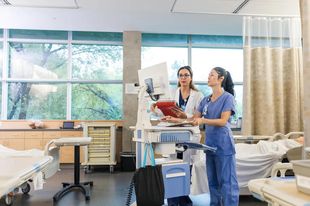 Two clinicians reviewing a bedside computer cart in a hospital room